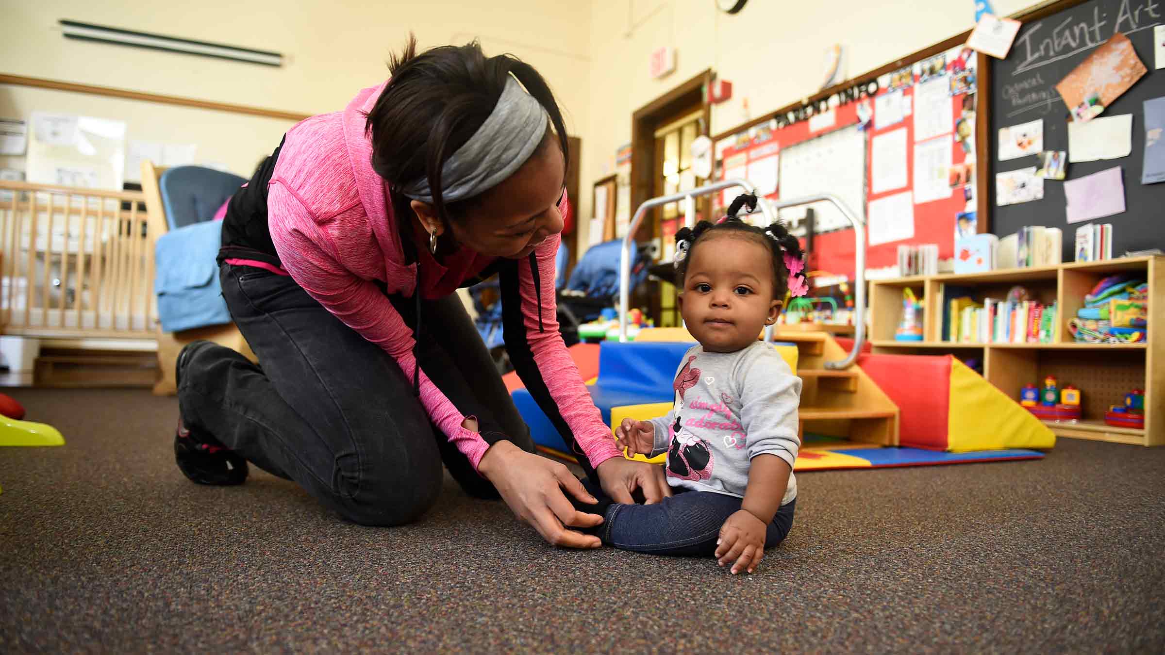 A mother is gazing affectionately at her child who is seated inside a preschool classroom