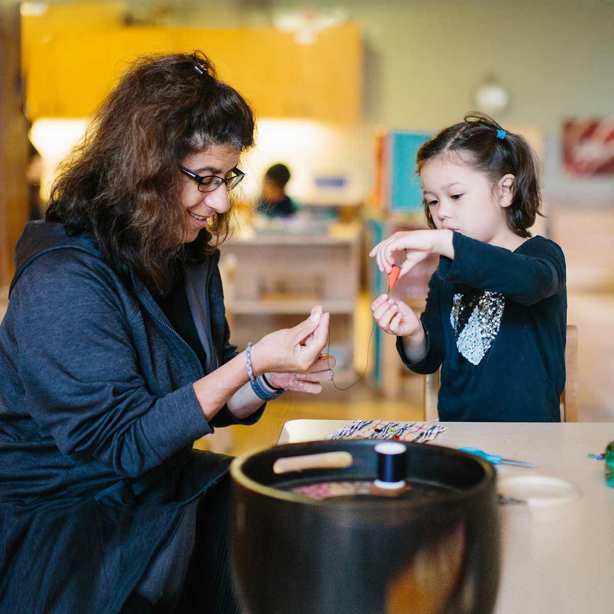 A teacher is showing her student how to unwind a spool of thread